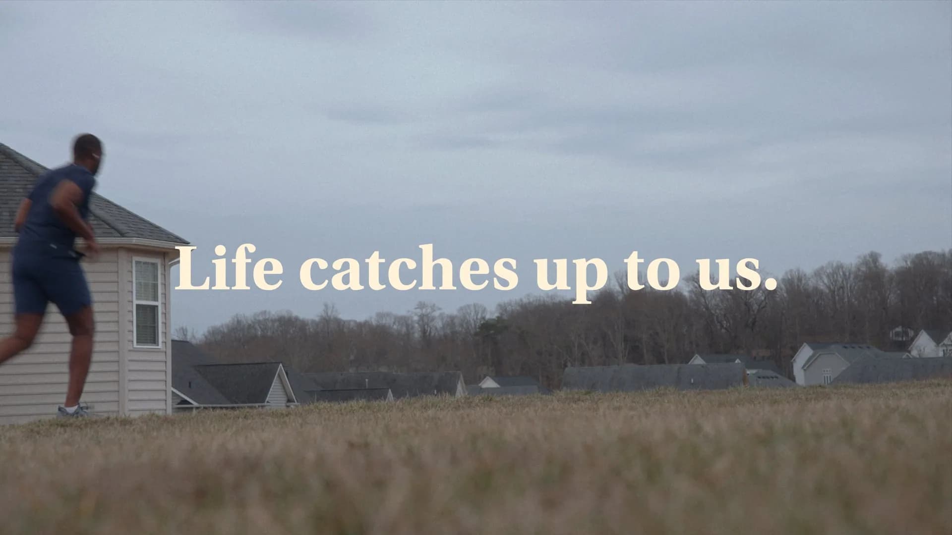 A still from the Healthy Beginnings campaign: a man running past suburban houses, captioned “Life catches up to us.”