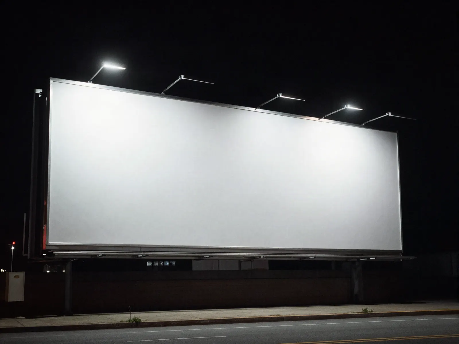 A blank billboard standing over an empty street at night under floodlights.
