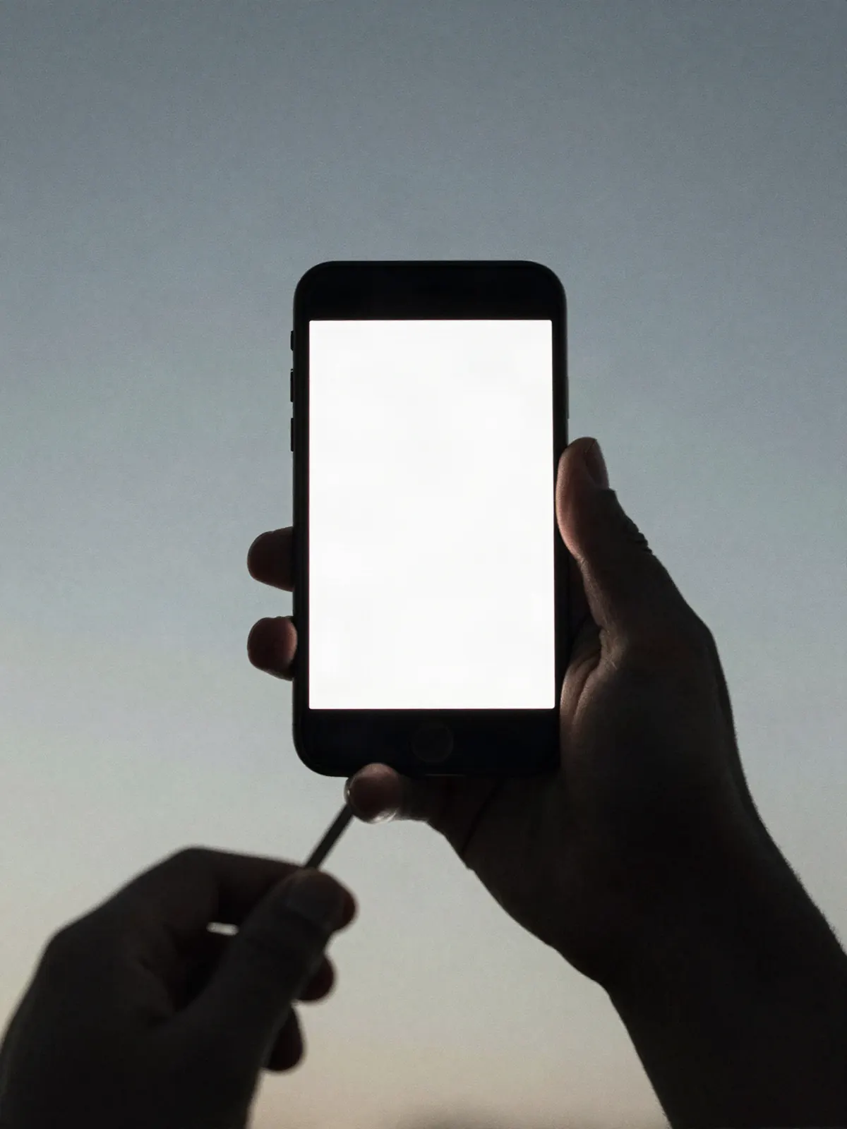 A hand holding a phone up in flat daylight, the screen blown out to pure white.