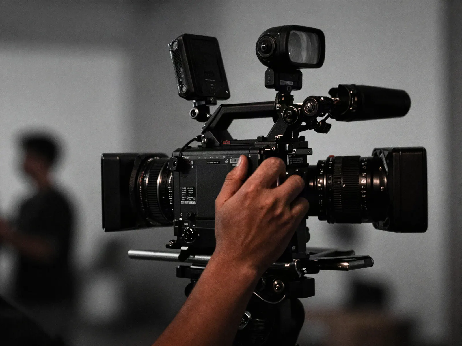 A camera operator's hands gripping a cinema camera on a shoulder rig, the location behind melting into light.