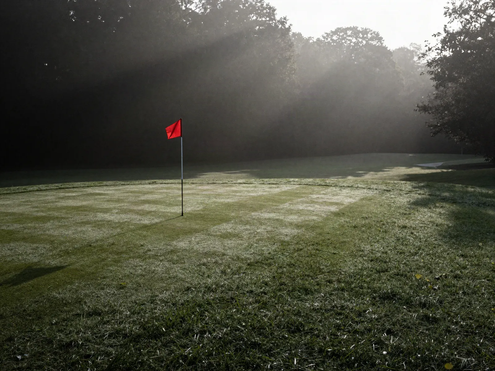 Early morning on a golf fairway with mist sitting on the grass and a flagstick catching first light.