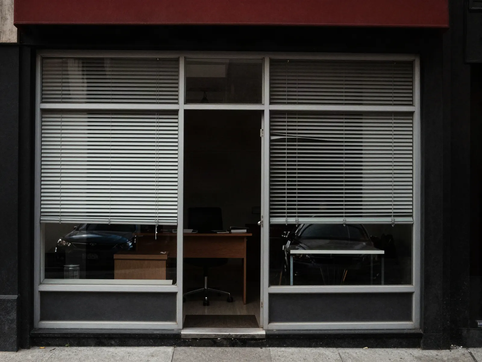 A small independent office storefront on a main street by day, blinds half open and a desk visible inside.