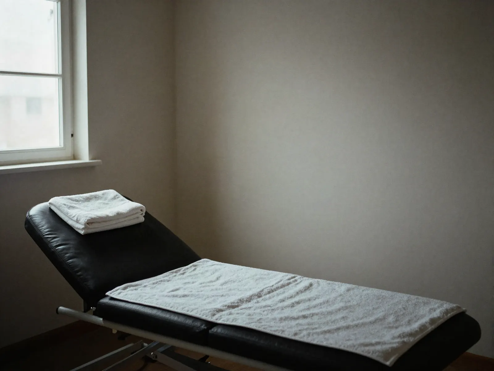 A quiet treatment room with a single reclining lounger, folded towels and soft window light.
