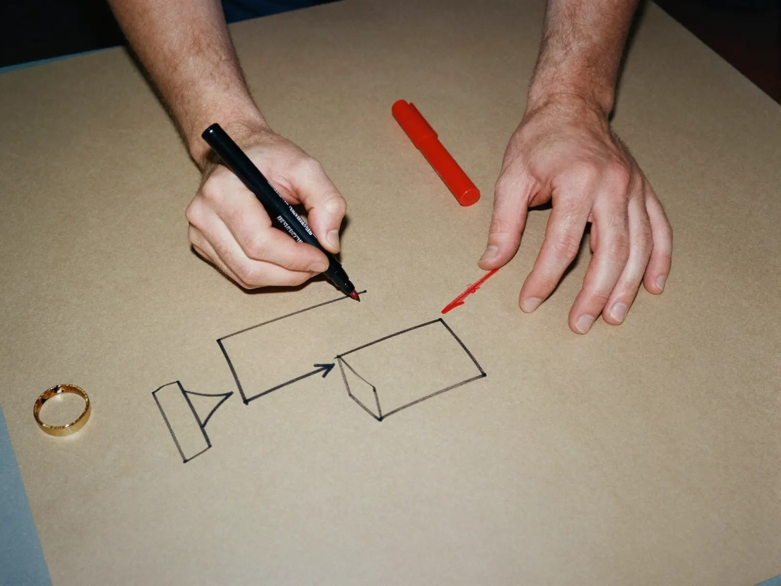 An overhead shot of two hands drawing a diagram of boxes and arrows on butcher paper with a black marker.